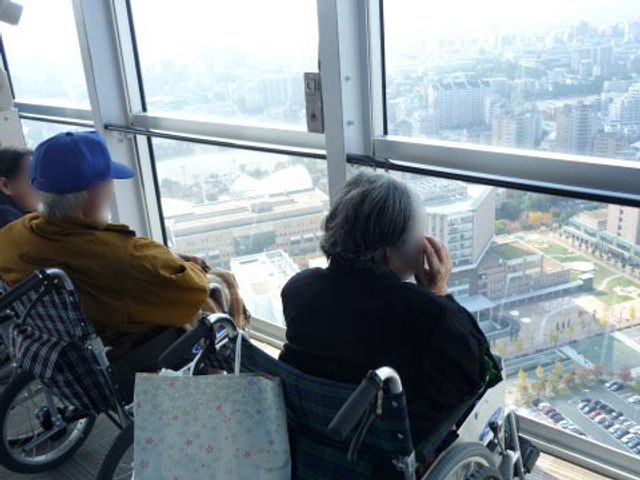 車椅子の人々と眺望 外出イベント 床から天井までの窓が開放的なラウンジです。都市の景色を一望でき、ゆったりとした時間を過ごすことができます。