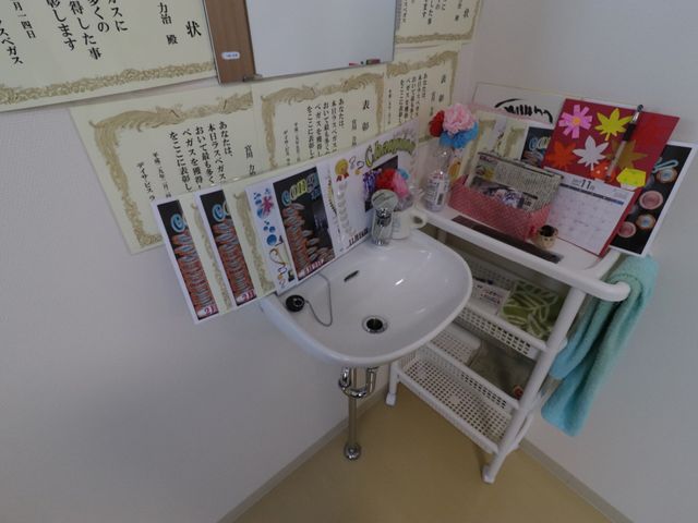 洗面台と掲示物の角 手洗い場 手入れの行き届いた清潔な洗面スペースです。壁に掲示された賞状やカレンダーが、居心地の良さを演出しています。