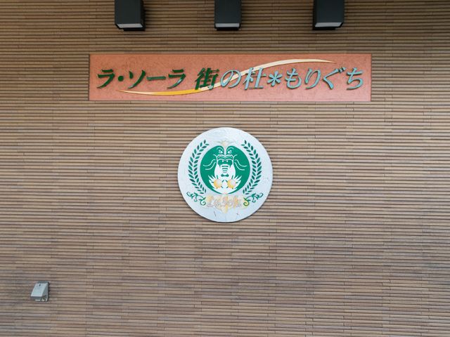 施設の看板とロゴマーク 看板 壁に取り付けられた看板には、施設名と緑豊かなロゴマークが描かれ落ち着いた印象を与えています。