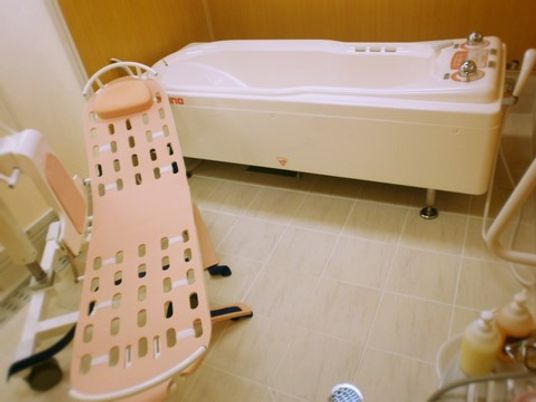担架に乗せた入居者様をキャスターで運び寝たまま介助入浴ができる固定式介護浴槽が置いてある。浴槽でずり込まないよう足部分が斜めになっている。