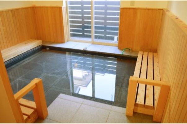窓が１つあり壁が木材でできている。３辺の壁に木製の椅子が設置され足湯のようにして入ることもできる浴室である。