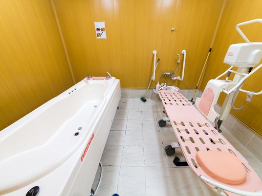 床はタイル、壁面は木目調で出来ている。寝た姿勢で身体を洗浄できる補助器具が設置されている。シャワーがあり、白い手すりが2箇所についている。