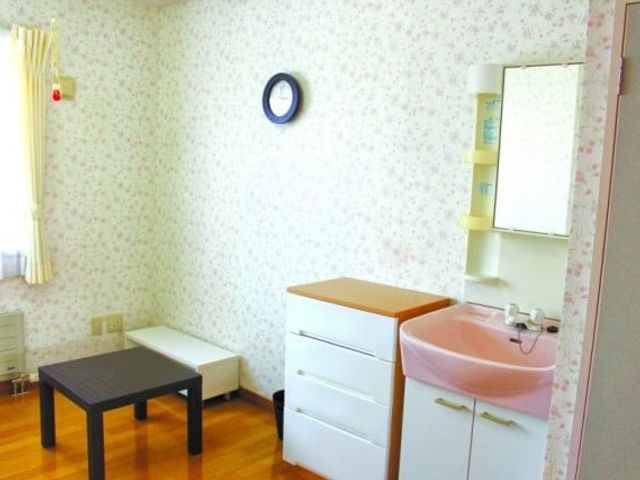 明るい居室の洗面台 居室   花柄の壁紙と木目の床が温かい雰囲気の居室です。洗面台や収納がまとまっており、身支度しやすそうです。