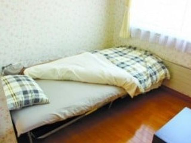 シンプルな居室のベッド 居室   窓からやわらかな光が入る、落ち着いた雰囲気の居室です。ベッドが整えられており、休息しやすい空間に見えます。