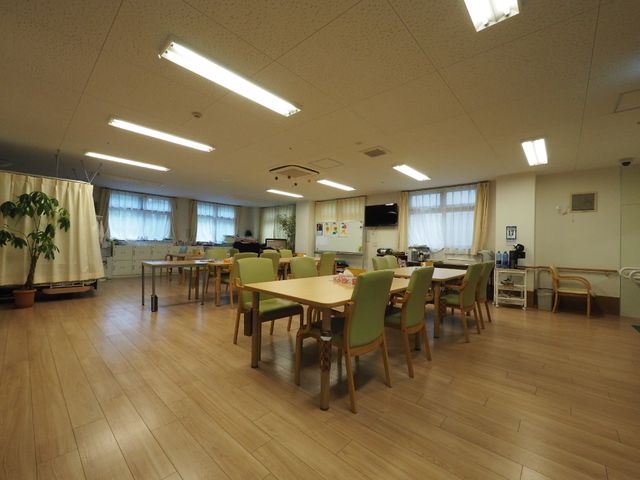 広々とした共用ダイニング 共有スペース ゆったりとした空間のダイニングルームでは、利用者が明るく快適に食事を楽しめます。後方にはスタッフの方が見守る姿もあり、安心感が伝わります。