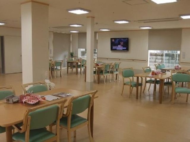 明るい共用ダイニング 食堂 ゆったりとしたダイニングで明るく開放感のある食事スペースがあり、壁にはテレビが設置されています。利用者の方々が食事やコミュニケーションを楽しむ場として配慮されています。