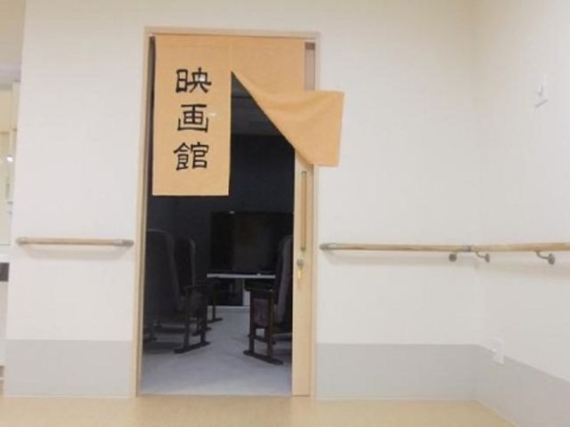 開かれた和室の扉 映画館 スライド式の和室入口は、利便性と安全を兼ね備えた造りになっています。木の温もりを感じる落ち着いた空間で、ご高齢者のくつろぎのひとときをサポートします。