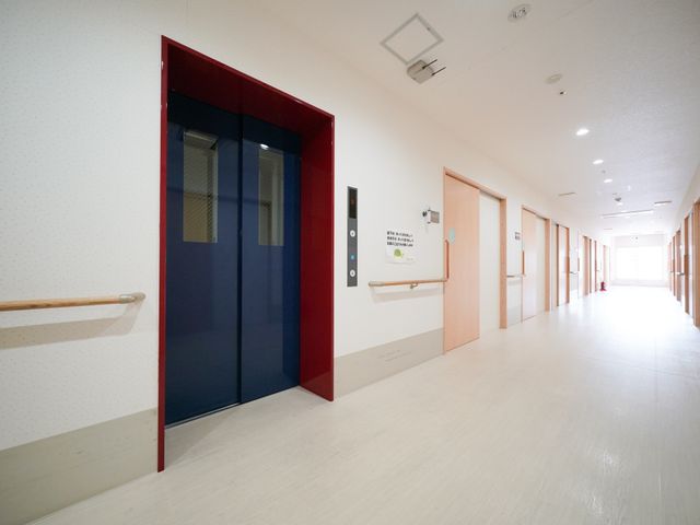 明るい廊下とエレベーター 共用廊下 手すりが設置された広々とした廊下です。明るく清潔感のある環境は、働くスタッフにとっても快適です。