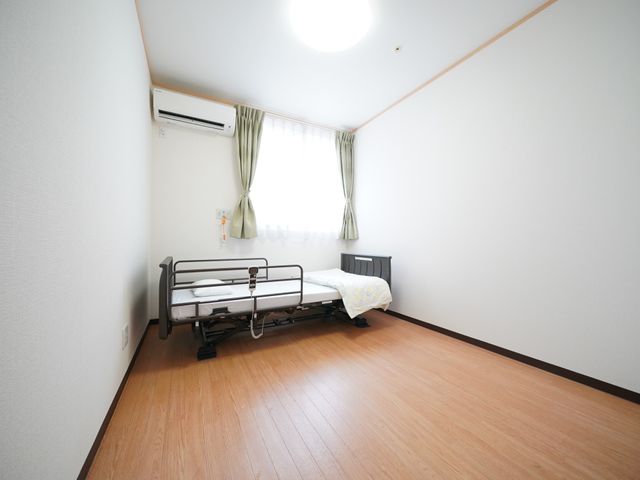 清潔な居室の一例 居室 広々とした居室は清潔感があり、大きな窓からは柔らかな光が差し込みます。安全を考慮したベッドや足元の広い空間も特徴です。