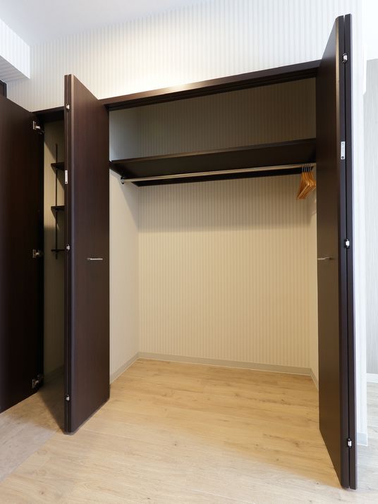 焦げ茶色の両開きの折り畳み式の扉の収納である。内部は、服を掛けれるようになり、上の部分に棚がある。隣にも細長い片開きの収納もある。