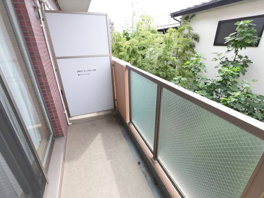 居室のバルコニースペースである。グレイの枠の針金入りすりガラスのフェンスである。隣との間には仕切りが取り付けてある。