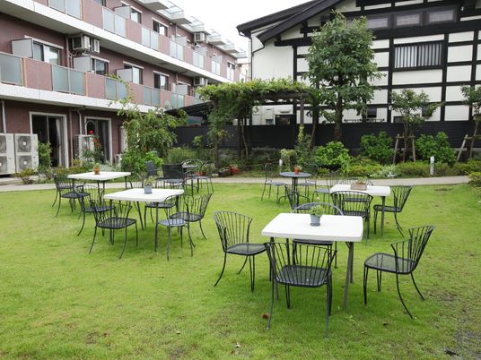 敷地内には、施設の建物の隣に古民家風のレストランがあり、その傍には芝生が敷き詰められたスペースがある。テーブルや椅子が置かれている。