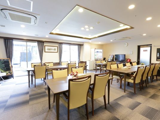 白色の天井と壁にデザイン仕様の床の内装である。テーブルと椅子が並べてあり、横面はガラス戸である。テレビが置かれ、自動販売機が設置されている。