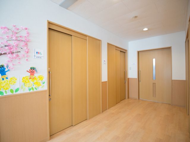廊下の明るい居室入口 廊下 色とりどりの手作り装飾が廊下に彩りを加え、訪れる方々に明るく温かい印象を与えています。ゆったりとした出入口は利便性を考慮して設計されています。