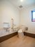 トイレには、温水洗浄便座器と可動式手すりが設置されている。側面の壁にはL字型手すりや手洗い器が取りつけられている。
