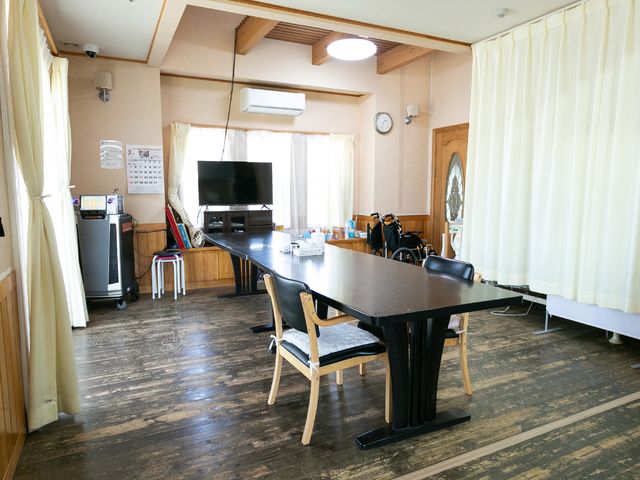 温かみのある居室空間 共用スペース 木の温もりを感じる共有スペースには、くつろぎや交流が生まれる大きなテーブルがあります。車椅子の方も一緒に過ごせる広々とした設計です。