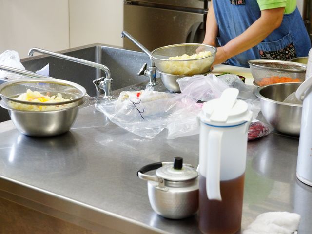 キッチンで調理中の様子 キッチン 清潔なキッチンで、栄養満点の食事を提供する準備が行われています。食材の手入れをする職員の姿が見られます。