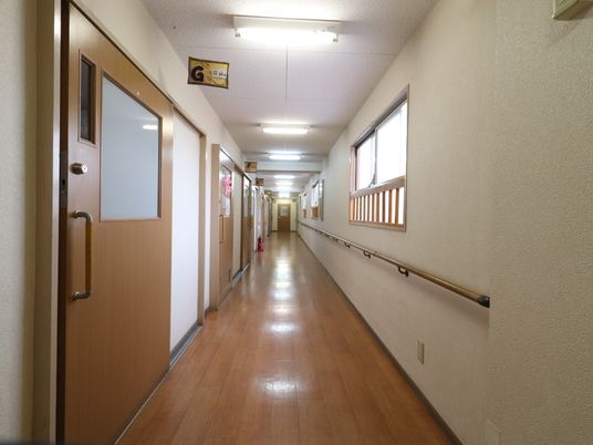 施設の写真 廊下の両サイドの壁には手すりがあり、掴まりながら歩くことができ便利である。部屋があり、大きなハンドルがついた扉なので、開閉が楽である。