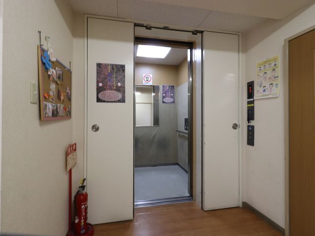 廊下にあるエレベーター エレベーター ゆったりとした空間の廊下に、待ち時間も快適に過ごせるエレベーターが設置されています。掲示物があり、コミュニケーションの場も提供しています。
