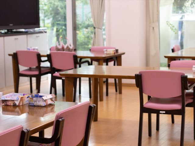 ピンクの椅子が並ぶ食堂 食堂 窓際の明るい食堂は、ピンク色の椅子が配置され、暖かい雰囲気を醸し出しています。利用者様がゆったりと食事を楽しめる空間です。