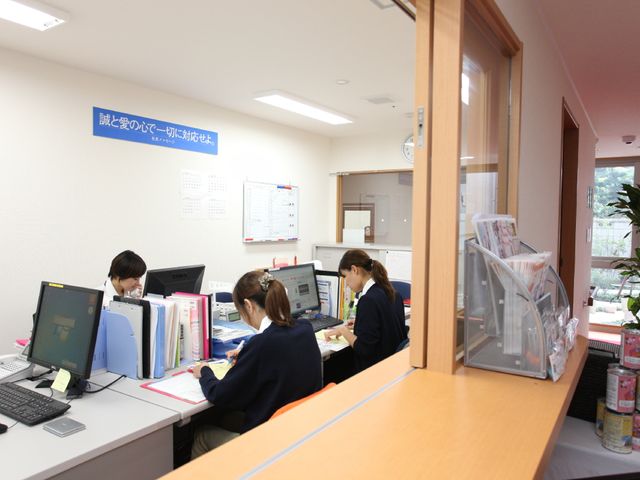 スタッフ作業中のフロント 事務所 丁寧に業務をこなすスタッフの姿は、訪れる方々に安心感を与えます。チームワークで支え合う職場環境をお探しの方に最適です。
