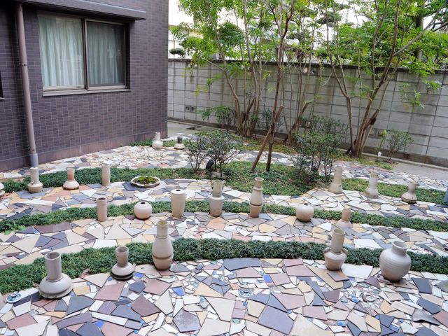 陶芸作品が並ぶ中庭 エントランス側から見た中庭 施設には創造性を養う陶芸作品が飾られた中庭があり、利用者の心を和ませる空間となっています。美しく配置された作品は、働く人々にも癒しを提供します。
