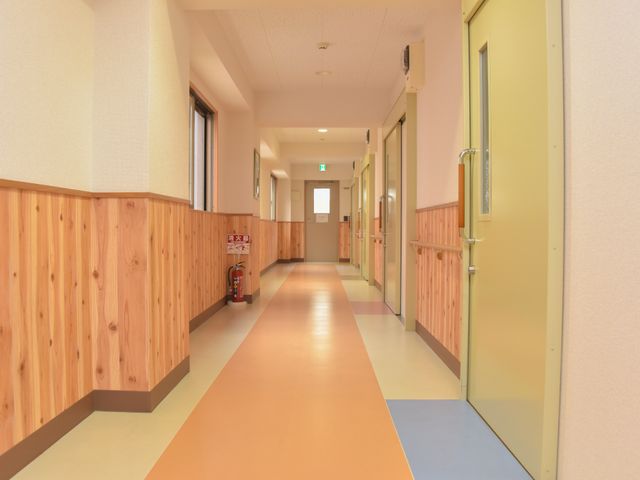 清潔感ある施設の廊下 廊下 木目調の壁とやわらかな色彩の床が穏やかな雰囲気を演出する廊下です。明るく開放感ある設計で、安心して過ごせる環境を提供しています。