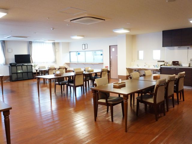 広々とした共有スペース 食堂 床の木目が温かみを感じさせる明るい食堂です。テレビを見ながらくつろぐことができ、憩いの場となっています。