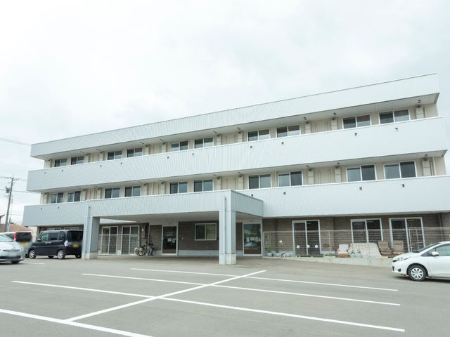 白い建物の外観 充分な駐車スペース 広々とした駐車場が完備された明るい建物です。仕事へのアクセスも快適になっています。