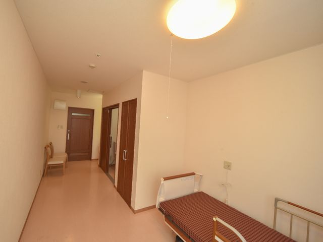 シンプルな居室内観 個室の出口部分 ベッドとイスを備えた居室は、シンプルで清潔感があり、個人のスペースを大切にできる落ち着いた環境です。