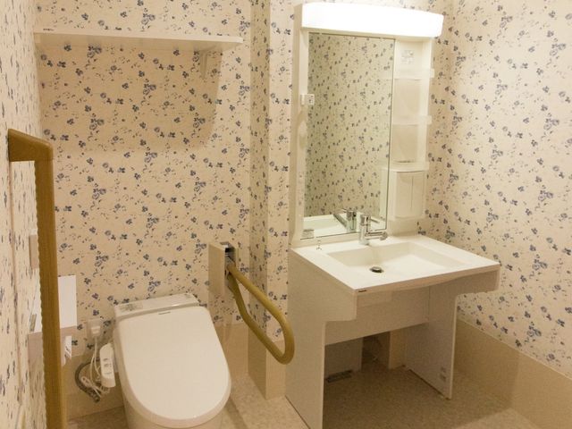 バリアフリー対応の洗面台 トイレ 手すり付きのトイレは、安全性を考慮した設計です。清潔感のあるデザインで、利用者の方々の快適な生活をサポートしています。
