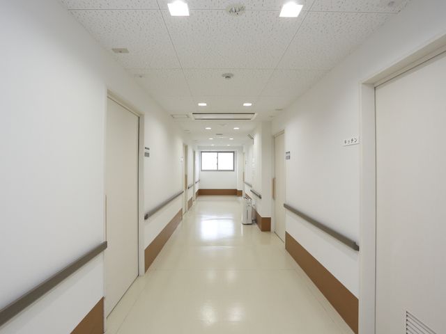 清潔な施設の廊下 明るい廊下 広々として明るく、清潔感が漂う施設の廊下です。壁には手すりが設置され、安全に歩行できるよう配慮されています。