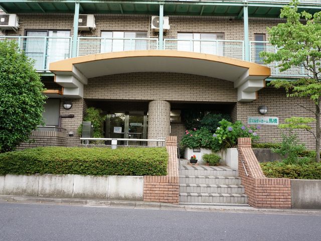 緑に囲まれた建物入口 施設入り口 植物に囲まれた落ち着いたエントランスです。訪れる方を優しく迎え入れる、心安らぐ雰囲気が感じられます。