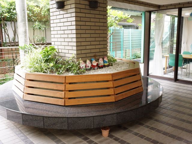 中庭の円形花壇 エントランス ガラス越しに見えるテーブル席が並ぶ社交的なスペース。緑に囲まれた円形花壇が潤いと癒しを提供しています。