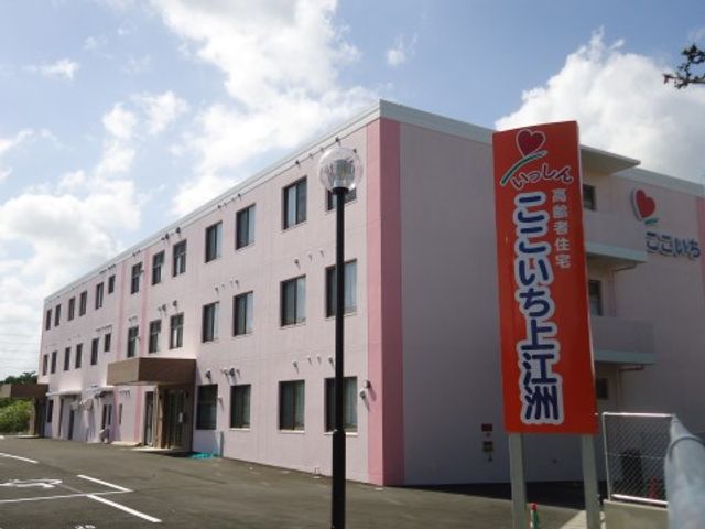 ピンクの壁の建物と看板 施設外観 ピンク色を基調とした外壁が印象的な施設で、明るい雰囲気が感じられます。駐車場も完備しており、通いやすい環境です。