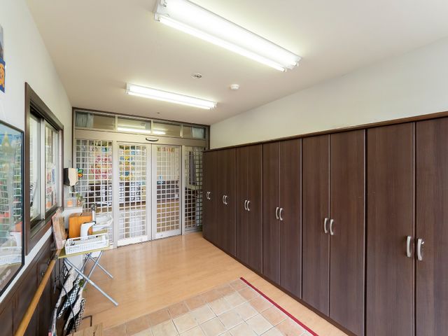 収納棚と入り口の廊下 玄関 広々とした明るい廊下には、利用者様の私物を収納するための多くの木製のロッカーが整然と並んでいます。