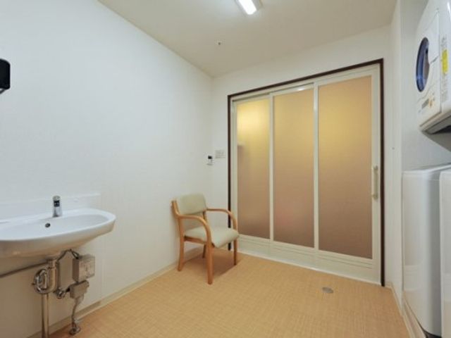 清潔な洗面所と椅子 脱衣所 使用しやすい洗面台と休憩できる椅子が配された静かな空間です。利用者の快適な生活をサポートする設備が整っています。