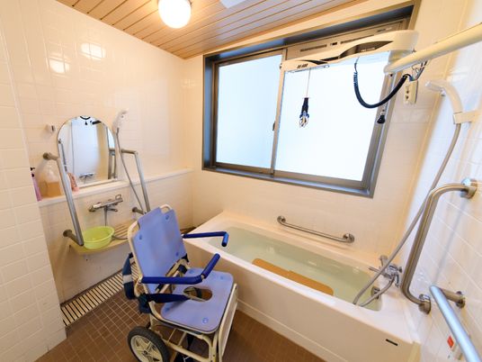 大きな窓があるタイル張りの浴室にはゆったりとした広さがある浴槽が置かれ、リフト式の入浴機器が設置されている。