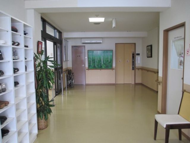 清潔な廊下と植物 エントランスホール 広々とした明るい廊下が安心感を与え、植物が温かな雰囲気を醸し出しています。椅子も配され、待機や休憩にも適しています。