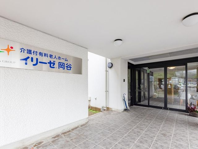 木製家具の明るい食堂 外観エントランス 広々とした食堂で、利用者が明るい日差しの中、くつろいでいます。木の温もり溢れる家具が、暖かい雰囲気を醸し出しており、やすらぎの時間を過ごせる空間です。