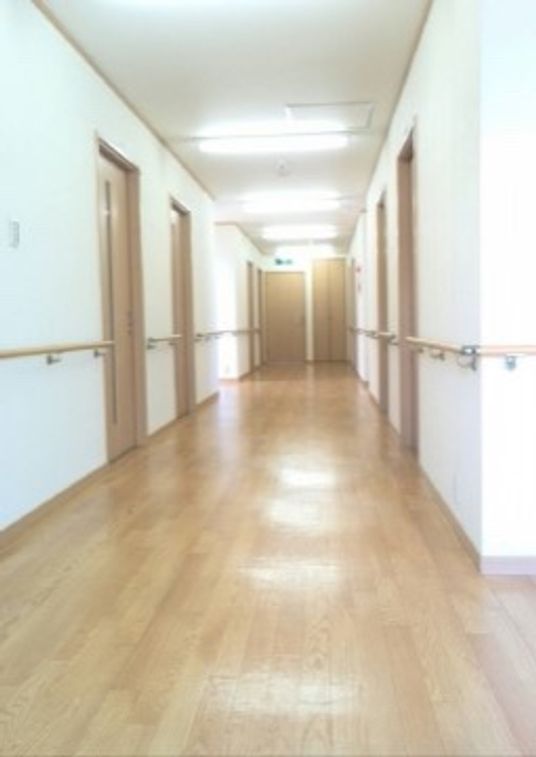 光沢がありきれいなフローリングの廊下は余裕のある広さで作られている。左右の白い壁には手すりが設置されている。