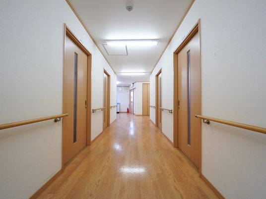 木目調がくっきりと出ている、光沢のある明るい床の廊下がある。両サイドには入居者様の居室のドアが並んでいる。