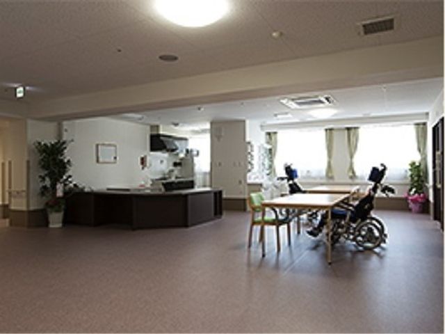 車椅子利用者の食堂 ロビー 広々としたダイニングルームで、車椅子の方がテーブルに向かっています。窓からの自然光が心地よい明るさを提供しており、居心地の良い雰囲気です。