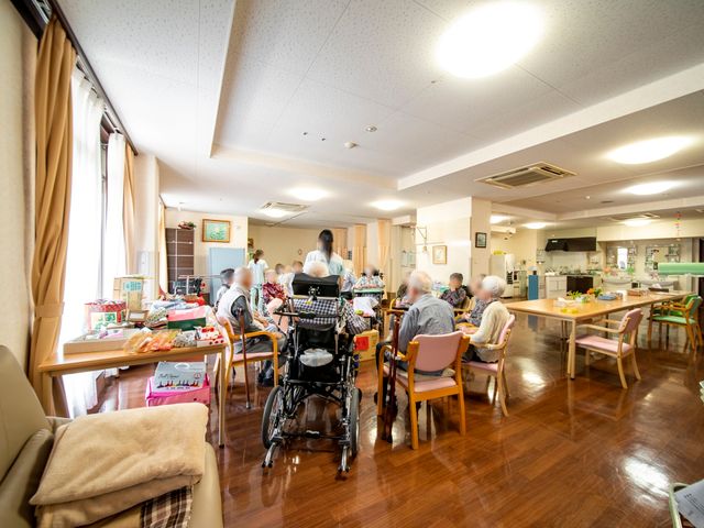明るい共有スペース 食堂 ゆったりとした食事のひとときを支えるスタッフが見えます。温かい日差しを感じる食堂で、利用者さまが団らんされています。