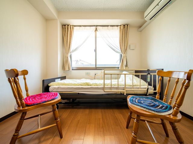 居室の明るい光景 ベッド 明るい窓辺と手作りのクッションが心地よい居室です。木の温もりを感じる家具が配置されています。