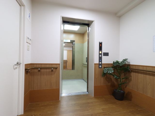 廊下にあるエレベーター エレベーター 床材と木目の壁が落ち着いた雰囲気を演出するエレベーターホールです。スタッフとして働く方々の移動にも配慮された設計になっています。
