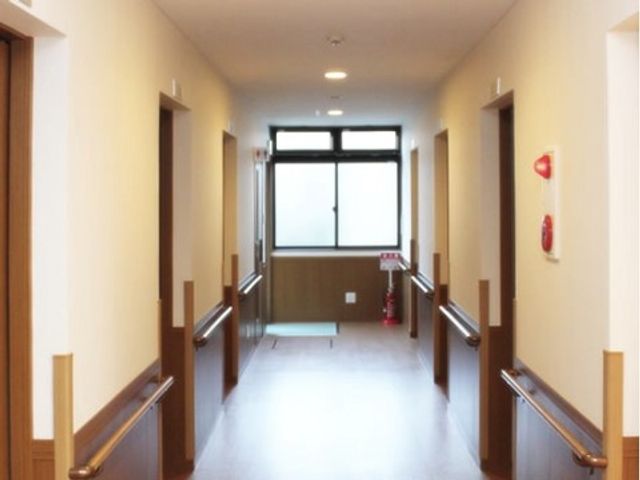 手すり付きの明るい廊下 廊下 壁に設けられた手すりが廊下の両側に続いており、安全に配慮された明るい通路をご利用いただけます。突き当たりの窓からは自然光が差し込み、開放感のある環境が広がっています。