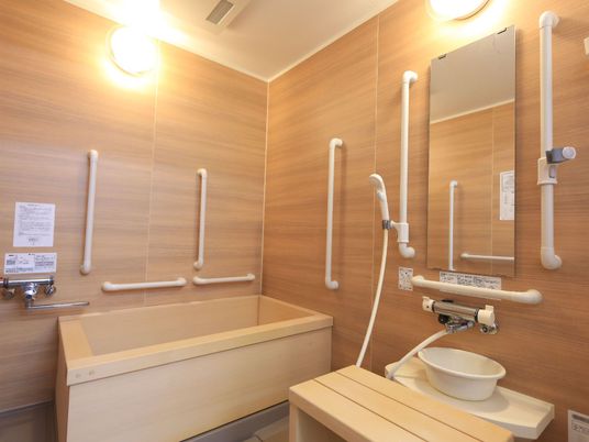 施設の写真 ひのき風呂タイプの浴室。浴槽の材質に合わせて、カラン前のバスチェアもすのこ型の木製のものになっている。