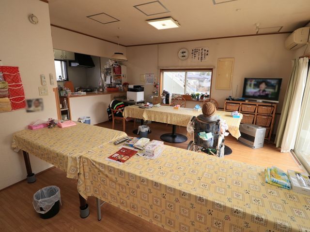 居室の明るい空間 共有スペース ゆったりとしたリビングで、テレビを視聴しながらリラックスしている方がいらっしゃいます。日当たりの良い窓辺で、ゆっくりとした時間を過ごせるのが魅力です。