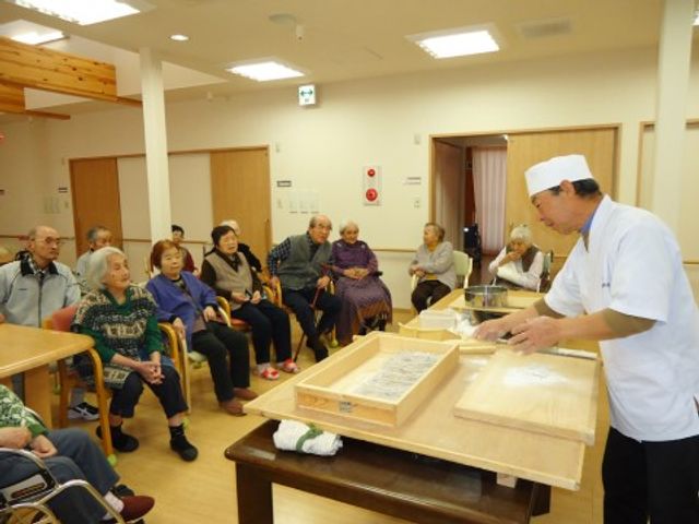 料理実演のある共有スペース 共有スペース 料理人が実演する様子を見守る利用者の表情が和やかです。この様な交流は、日々の暮らしに彩りを与えているようです。